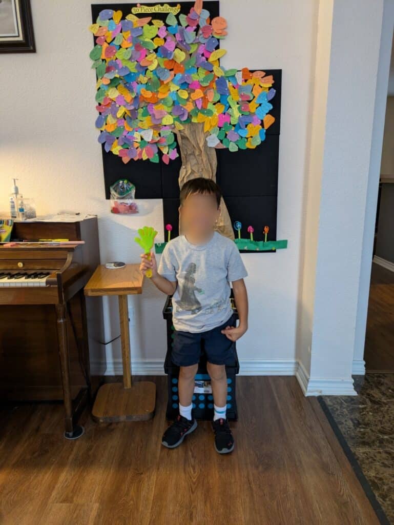 Image of a smiling child holding an award in front of the studio decoration and incentive tree.